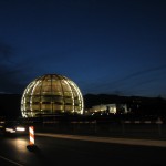 Yöllinen CERN. Etualalla Globe, jonka takana on valaistuna Atlas-koeaseman rakennukset. Taustalla aurinko laskee Jura-vuorten taakse.